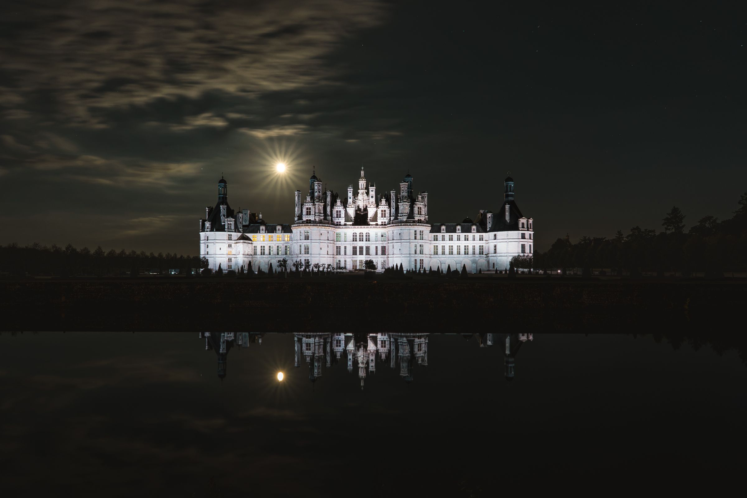 An illuminated château under a full moon at night